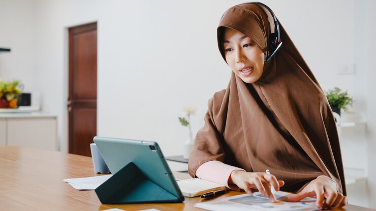 Female Quran teachers wearing a hijab, using a tablet and headset while teaching online from home, Female Quran teachers, Quran learning for women, Online Quran learning Quran classes online Learn Quran online Quran tutoring services Online Quran teaching Best online Quran courses